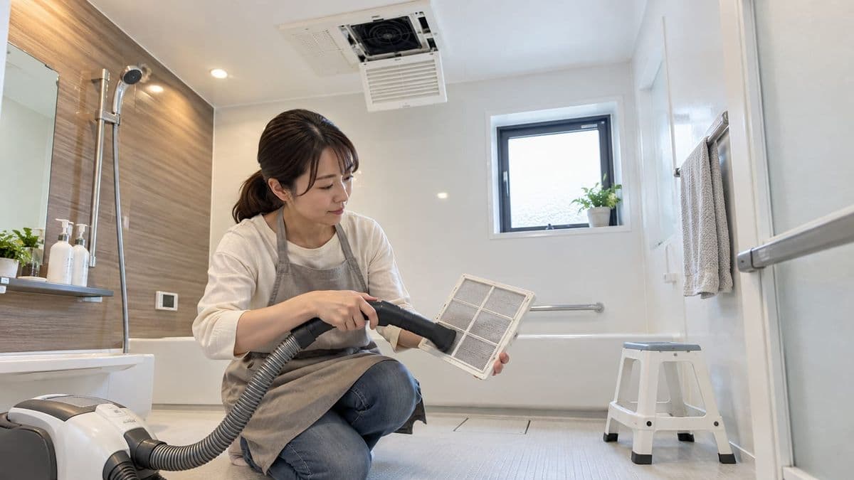 浴室暖房乾燥機の外したフィルターを床で掃除する人